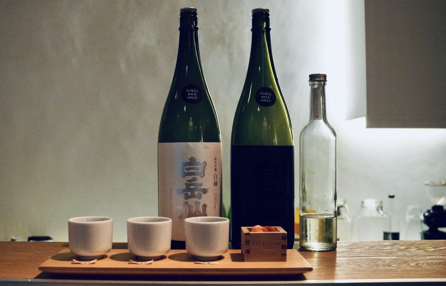 A flight of sake with two large bottles and three wooden tasting cups