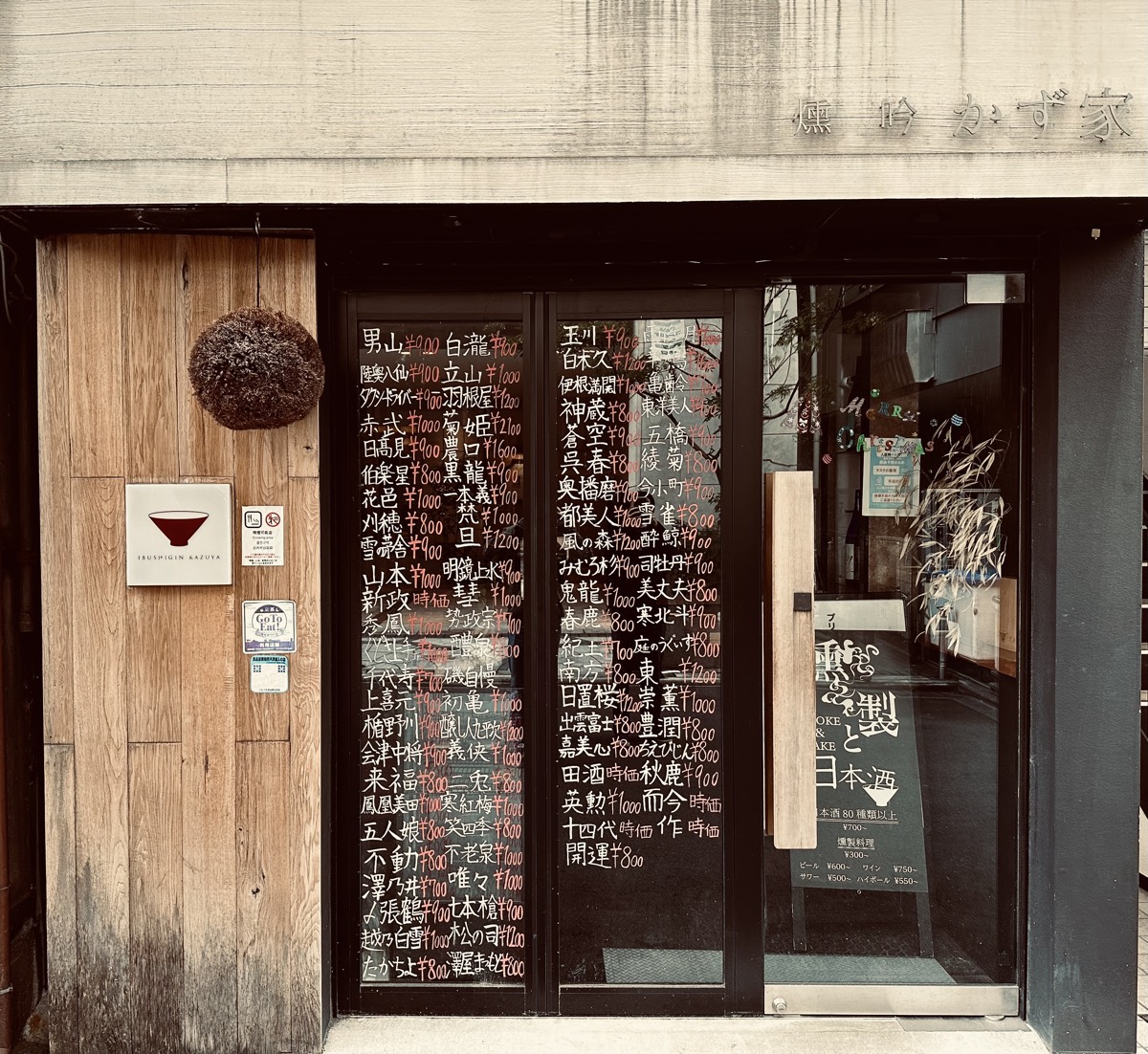 A sake bar storefront, its glass door covered in handwritten sake names